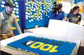  ?? NWA Democrat-Gazette/CHARLIE KAIJO ?? Brandon Eddins (left) of Bentonvill­e unveils the centennial cake Thursday at The Walmart Museum.