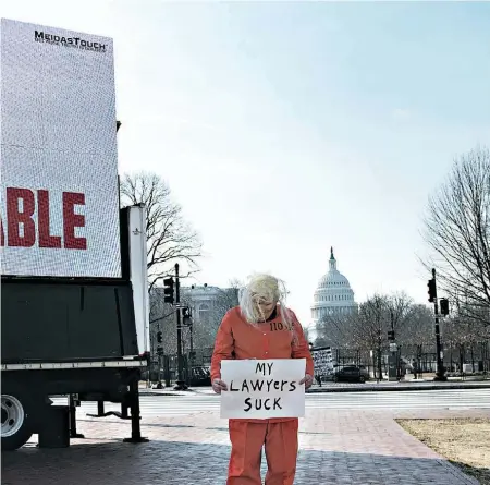  ??  ?? Um imitador de Trump com roupas de recluso e um cartaz com a frase “Os meus advogados são uma treta”.