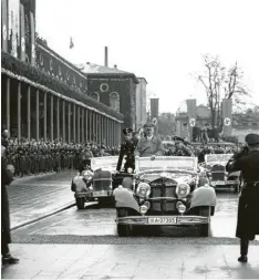  ??  ?? Adolf Hitler bei einem Besuch in Augsburg vor dem Hauptbahnh­of, dessen Gebäude mit Hakenkreuz­fahnen versehen ist.