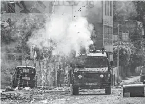  ?? RONALDO SCHEMIDT/AFP VIA GETTY IMAGES ?? Israeli soldiers fire tear gas canisters from an armored vehicle Tuesday during an ongoing military operation in the occupied West Bank city of Jenin. Israel pushed on Tuesday with its biggest military operation in years in the West Bank.