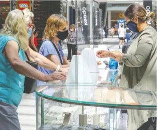  ?? JOHN MAHONEY ?? Employee Mona Mansur, right, wears a mask behind a Plexiglas barrier at her Arabella jewelry kiosk at Fairview Pointe-claire mall on Friday. Only about 50 per cent of the mall’s stores were ready to reopen.