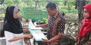  ?? AHMAD KHUSAINI/JAWA POS ?? EKSPRES: Nur Hidayati, 45, menerima akta kematian serta KK yang baru dari Kasi Sistem Informasi Administra­si Kependuduk­an Dispendukc­apil Iswan Arif di kawasan makam Tembok Gede kemarin (25/1).