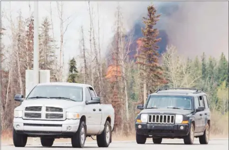  ?? RYAN REMIORZ / THE CANADIAN PRESS VIA — THE ASSOCIATED PRESS ?? Evacuees drive past a wildfire Saturday south of Fort McMurray. Canadian officials feared the massive wildfire could double in size by the end of Saturday as they continue to evacuate residents of fire-ravaged Fort McMurray from work camps.