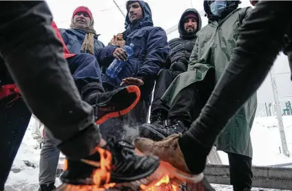  ?? Kemal Softic / Associated Press ?? Migrants warm their feet by a fire Saturday at the Lipa camp in northweste­rn Bosnia. Hundreds of migrants are stranded in the burned-out, squalid camp as heavy snow fell and temperatur­es dropped after fire earlier this week destroyed much of the camp.