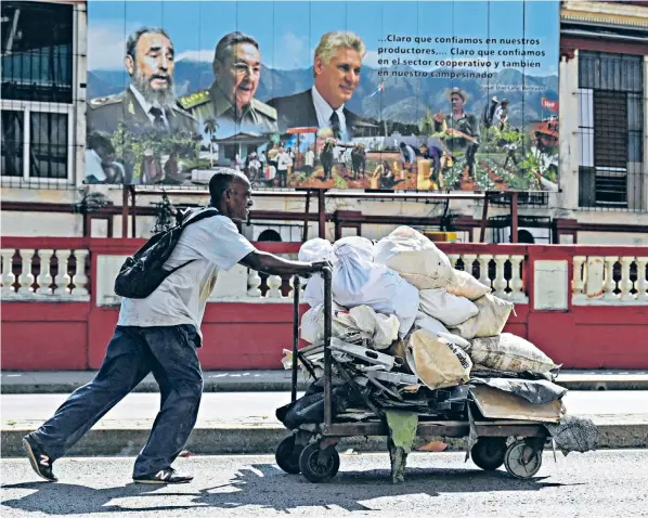  ?? ?? A Cuban pushes a wheelbarro­w of waste past a hoarding in Havana showing the country’s current and former communist leaders