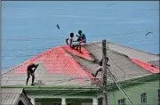  ?? (AP/Orvil Samuel) ?? People clean volcanic ash off the roof of a home Monday in Wallilabou on the western side of the Caribbean island of St. Vincent.