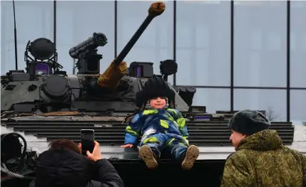  ?? Photo by Olga MALTSEVA / AFP ?? A woman takes a photo of a child sitting on a military vehicle during the Russians Change the World patriotic festival in Saint Petersburg on February 24, 2024, on the second anniversar­y of the Russian invasion of Ukraine.
