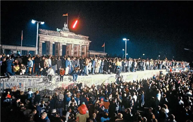  ?? GETTY IMAGES ?? The Berlin Wall in front of the Brandenbur­g Gate on the night of November 9, 1989. Thousands of celebrants climbed on the Wall as news spread rapidly that the East German Government would start granting exit visas to anyone who wanted to go to the West. The announceme­nt was misinterpr­eted as meaning the border was now open.