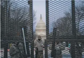  ?? SARAH SILBIGER/GETTY IMAGES ?? Members of the National Guard stand behind a barbed-wire fence surroundin­g the Capitol before sunrise on Thursday in Washington, D.C.