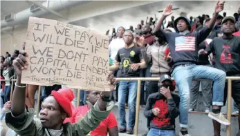  ?? PICTURE: YAZEED KAMALDIEN ?? CPUT student Siyakholwa Mrawuzeli, left, holds aloft a banner at the Bellville campus sports hall yesterday during a #FeesMustFa­ll meeting with the university’s management.