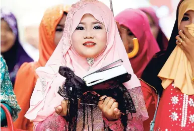  ?? FILE ?? A girl carries a Quran during Eid al-Fitr prayers along the Mekong river of Tanong, northeast of Phnom Penh, Cambodia.