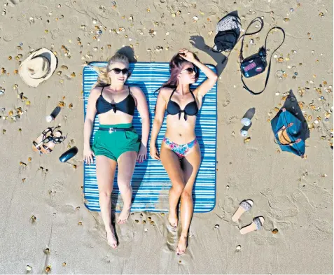  ??  ?? Alex Woolley, left, and Megan Young, both 22, from Cirenceste­r, sunbathe on Bournemout­h beach yesterday after temperatur­es soared at the start of the Easter weekend. The Met Office forecast highs of up to 77F (25C) today and tomorrow and said the country could enjoy its hottest Easter Sunday, surpassing the record of 77.5F at the Solent in 2011