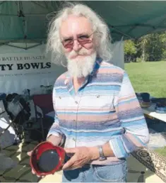  ?? ?? Phillip Calkins shows off a heart-shaped bowl, an original design that is special to him. Calkins has an artifical aorta, and felt lead to design a unique bowl for the Benton County Empty Bowls mission. The potter and retired certified public accountant heads up marketing and recruiting for the Bella Vista-based nonprofit.