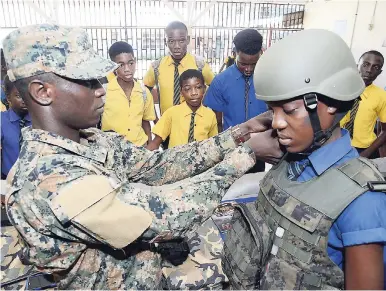  ?? FILE ?? In this June 2, 2017 photograph, Lance Corporal Doaneye Francis of the JDF fits a helmet on student Kelly Green’s head at Denham Town High School’s Career Health and Wellness Fair.