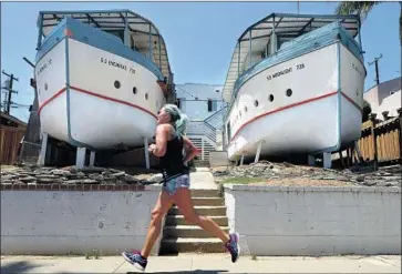  ?? Hayne Palmour IV San Diego Union-Tribune ?? A WOMAN JOGS past the Boat House apartments, located on 3rd Street in Encinitas, Calif. The structures are thought to be among the earliest and best examples of recycled architectu­re on the West Coast.