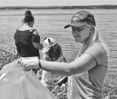  ?? ARDELLE REYNOLDS • CAPE BRETON POST ?? Karina Doucette holds the garbage bag while Oksana Doucette and Maxine Doucette pick up garbage on the shore in Potlotek First Nation. Oksana said she wanted to help out her community on National Indigenous Peoples Day on Monday.