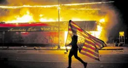  ?? —AP ?? DISTRESS A protester carries a US flag upside down next to a burning building in Minneapoli­s on Thursday.