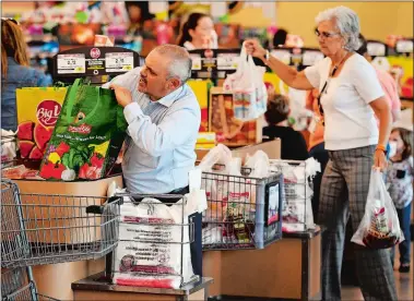  ?? SEAN D. ELLIOT/THE DAY ?? Ray Lathrop, left, store director for the Big Y in Groton, bags groceries Friday using a customer’s reusable shopping bag as Janet Smith, back, bags with single-use plastic for another customer.