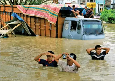  ?? ?? People wade past an inundated lorry stuck in floodwater­s in Lhoksukon, North Aceh, Indonesia on January 3, 2022, following heavy rainfall in the region.