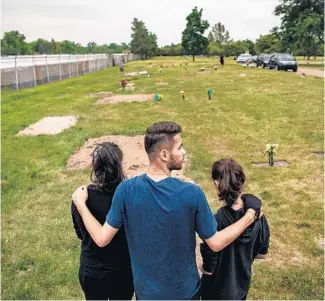  ?? SALWAN GEORGES/THE WASHINGTON POST ?? Nash Ismael, 20, puts his arms around his sisters Nadeen, 18, left, and Nancy, 13, as they visit the gravesite of their parents on Father’s Day at White Chapel Memorial Park Cemetery on June 21, 2020, in Troy, Michigan. The Ismael children lost both their parents within weeks to COVID-19.