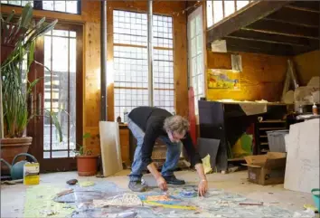  ?? Jessie Wardarski/Post-Gazette photos ?? Artist James Simon bends down to assemble the face of a bike rider in his latest glass mosaic mural, “The Magic River.” Mr. Simon cuts a piece of glass into the shape of an ear as he works to assemble “The Magic River,” which will be installed in Bradenton, Fla.