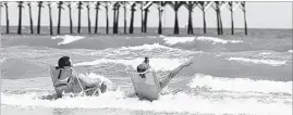  ?? CHUCK BURTON/ASSOCIATED PRESS ?? Vacationer­s sit in chairs in the surf at Oak Island, N.C., site of two separate shark attacks on June 14. A 12-year-old girl from Asheboro lost part of her arm and suffered a leg injury, and a 16-year-old boy from Colorado lost his left arm about an...