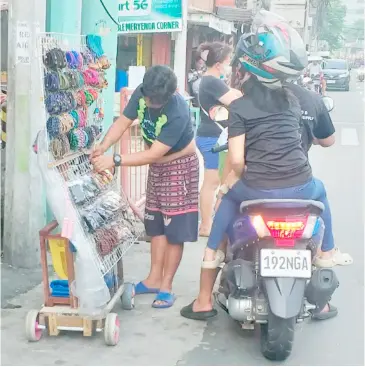  ?? PHOTOGRAPH BY JON GAMBOA FOR THE DAILY TRIBUNE ?? A MOTORCYCLE rider and his passenger check on bracelets being peddled by an ambulant vendor along a street in Caloocan City on Thursday afternoon.