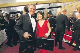  ?? Al Seib Los Angeles Times ?? WELL BEFORE THE CEREMONY, Brian Cullinan and Martha Ruiz of the Pricewater­houseCoope­rs firm were all smiles on the red carpet holding suitcases containing the winners envelopes.