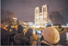  ?? KAMIL ZIHNIOGLU/ASSOCIATED PRESS ?? Tourists and others take pictures of Notre Dame cathedral in Paris on Monday. The cathedral, which was heavily damaged by a fire in April, is closed this Christmas for the first time in more than 200 years.