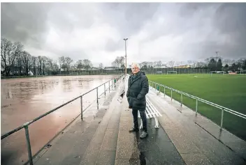  ?? FOTO: ABR ?? Das alte Tennenspie­lfeld links, der Kunstrasen rechts: Norbert Fischer, Geschäftsf­ührer des SV Wersten 04, steht auf der Anlage am Dechenweg. Dort soll das rotbraune Feld in ein weiteres Kunstrasen­spielfeld umgebaut werden.