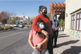  ?? Yalonda M. James / The Chronicle ?? Wearing masks to protect against the coronaviru­s, Yesenia Guzman and her daughter, 10yearold Lesly, wait in line to enter the T. J. Maxx store at South Shore Center in Alameda.