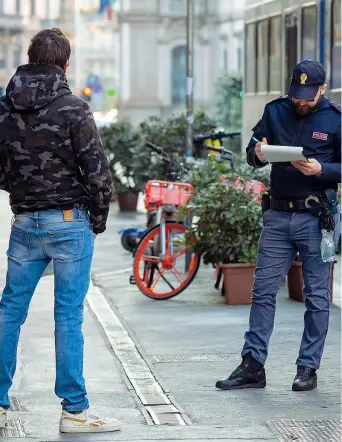  ??  ?? A Milano un poliziotto controlla un giovane a passeggio per le strade del centro nell’ambito delle disposizio­ni anti contagio