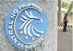  ??  ?? A security guard stands beside a logo of the Bangko Sentral ng Pilipinas (Central Bank of the Philippine­s) posted at the main gate in Manila, Philippine­s. Philippine President Rodrigo Duterte has tapped a China-backed multilater­al lender to help fund...