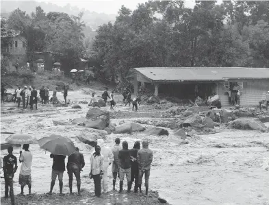  ?? SAIDU BAH / AFP / GETTY IMAGES ?? Bystanders look on as floodwater­s rage in Freetown on Monday, after landslides struck the Sierra Leone capital.