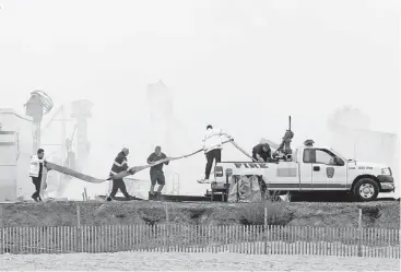 ?? Julio Cortez / Associated Press ?? Fire officials arrange a hose onto a pickup truck Friday as smoke rises from the Funtown Pier in Seaside Park, N.J., the morning after a fire burned a portion of the boardwalk that was rebuilt just months ago.