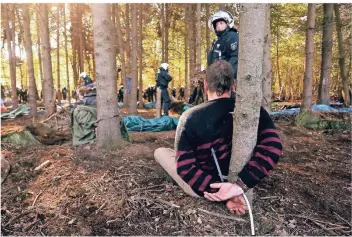  ?? FOTO: DPA ?? Ein Mann sitzt während eines Polizeiein­satzes im Hambacher Forst gefesselt an einem Baum. Vor ihm steht eine Polizistin. Sie bewacht den Aktivisten.
