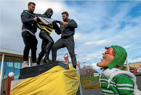  ?? PHOTO: MURRAY WILSON/STUFF ?? Manawatu Turbos prop Fraser Armstrong, left, and captain Heiden Bedwellcur­tis tear down some Wellington propaganda from the Charles Monro statue at the New Zealand Rugby Museum, while Turboman looks on.