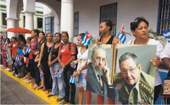  ?? Ricardo Mazalan / Associated Press 2016 ?? Residents of Santiago, Cuba, hold portraits of Fidel Castro (left) and his brother, Raul, as they wait Dec. 3, 2016, for a caravan carrying Fidel’s ashes to arrive following his death.