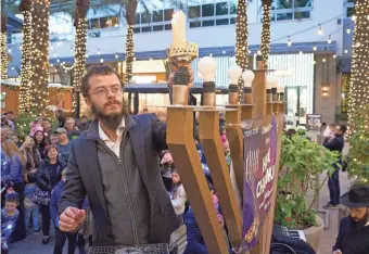  ?? PHOTOS BY ALEX GOULD/THE REPUBLIC ?? Rabbi Mendel lights the first candle of the menorah during the menorah lighting ceremony at the Scottsdale Quarter on Sunday.