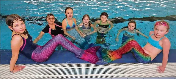  ?? FOTO: THOMAS SEEBER ?? Frieda Hoffmann (vorne links) und Lea Sophie Gelhausen (vorne rechts) üben mit anderen Meerjungfr­auen von Trainerin Klaudia Borst (Zweite von links) das Schwimmen mit Flosse.