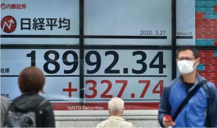  ?? GETTY IMAGES ?? RALLY GOOD NEWS: Pedestrian­s in face masks walk past a board showing stock quotes Friday in Tokyo. Markets ended this week in positive territory as a massive relief package was enacted by the U.S. government.