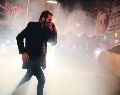  ?? MIDDLE EAST IMAGES / EP ?? Un joven se protege de los gases lacrimógen­os lanzados por la policía en Teherán la noche del sábado