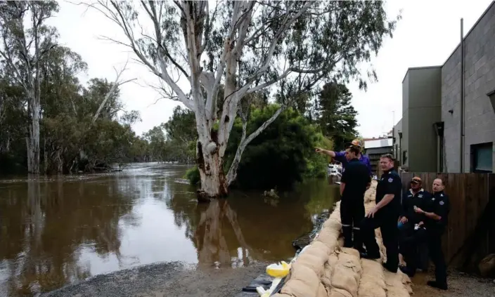  ?? Photograph: Mike Bowers/The Guardian ?? Firefighte­rs and locals survey sandbag levees as the water slowly rises to its flood peak in Echuca.