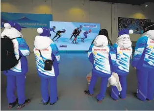  ?? DAVID J. PHILLIP AP ?? Olympic personnel watch a large television inside the main media center at the 2022 Winter Olympics on Saturday. There’s a pall over these Games due to pandemic and them being in China.