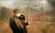  ?? AP PHOTO/JOHN LOCHER ?? Arianne Harvey holds her dog T.J. near a truck still on fire from the Camp Fire in Paradise, Calif. Harvey was living in an RV near where her family’s home was destroyed by the fire.