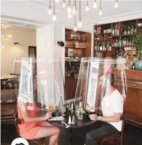  ??  ?? PATRONS UNDER PLASTIC. A man and a woman demonstrat­e dining under a plastic shield in a restaurant in Paris. As restaurant­s in foodloving France prepare to reopen, some are investing in lampshade-like plastic shields to protect diners from the virus. The strange-looking contraptio­ns are among experiment­s restaurant­s are trying around the world as they try to lure back clientele while keeping them virus-free.
