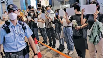  ?? | Reuters ?? PEOPLE hold white sheets of paper and flowers as police check their IDS during a protest over Covid-19 restrictio­ns in mainland China, during a commemorat­ion of the victims of a fire in Urumqi, in Hong Kong, yesterday.