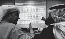  ?? Amr Nabil / Associated Press ?? Saudi traders chat as they follow a screen displaying stock values Thursday at the Arab National Bank in Riyadh, Saudi Arabia. State oil company Saudi Aramco hit $2 trillion Monday.