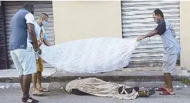  ?? AP ?? Neighbors cover the the body of a man who died of COVID-19 on a street in Rio de Janeiro, Brazil on Tuesday.