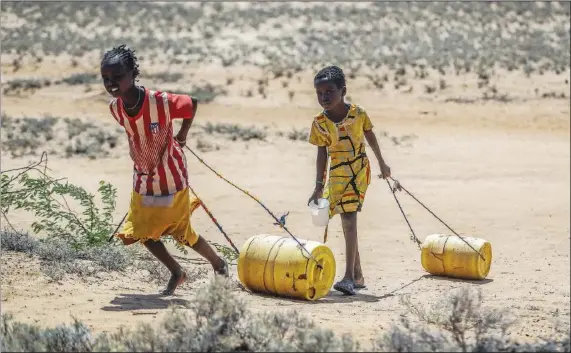  ?? (File Photo/AP/Brian Inganga) ?? Young girls pull containers of water May 12 during a drought as they return to their huts from a well in the village of Lomoputh in northern Kenya.